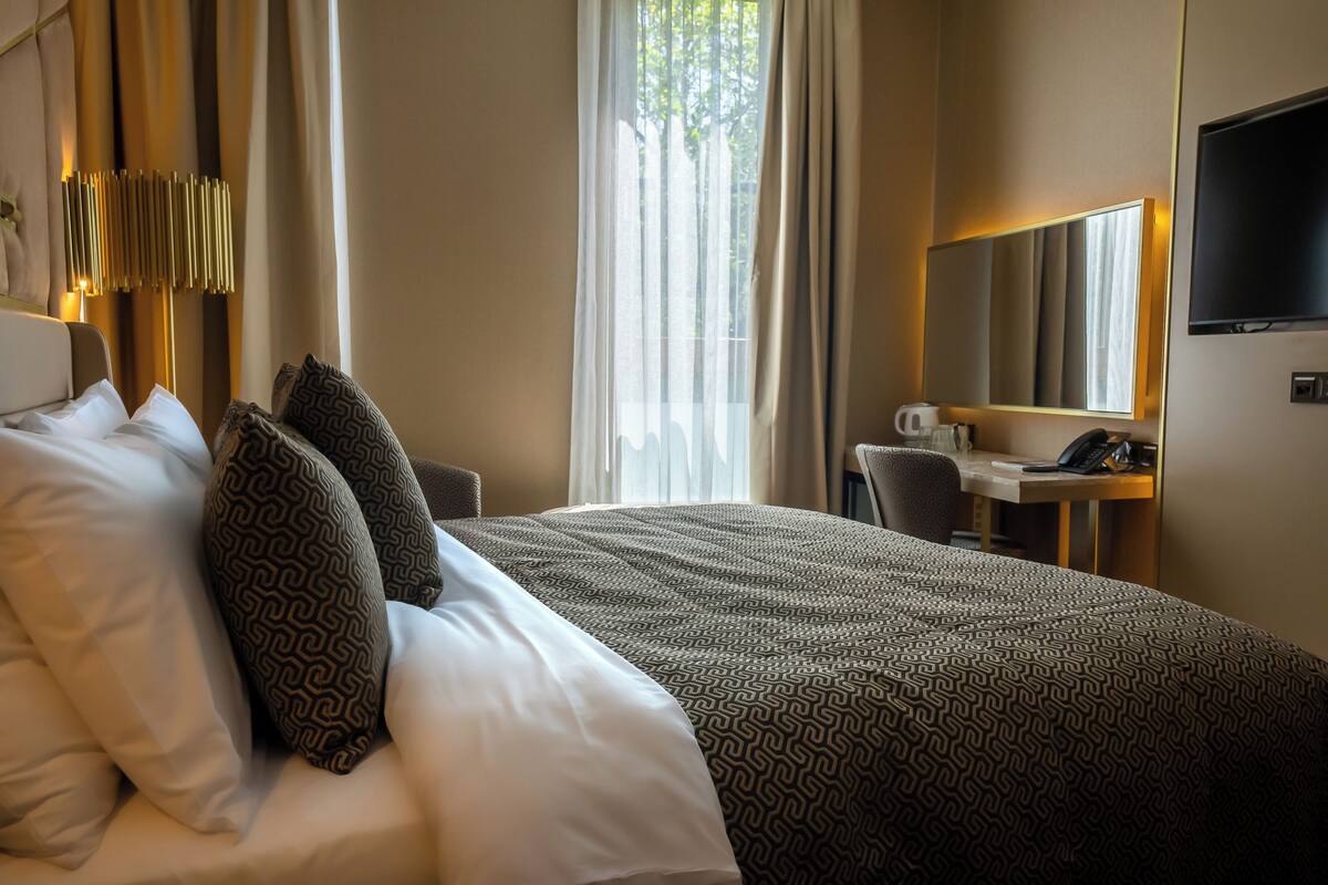 A hotel room with a large bed, a desk with a chair, a television, and a window with curtains.