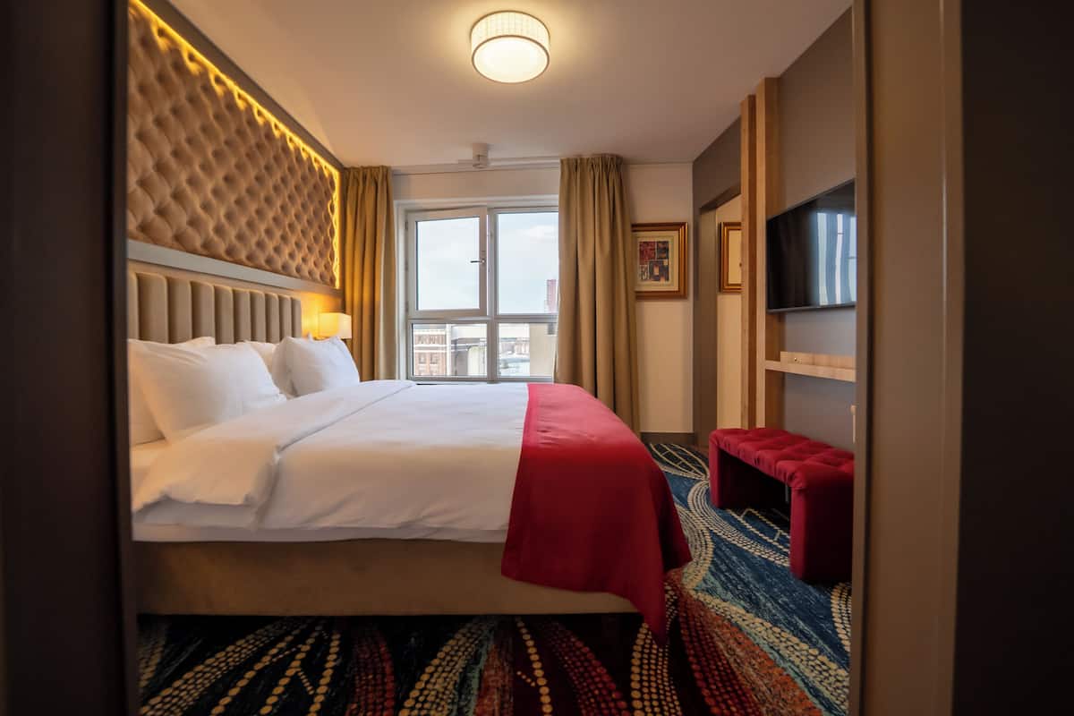 A hotel room with a large bed, a red bench, a television, and a patterned rug.