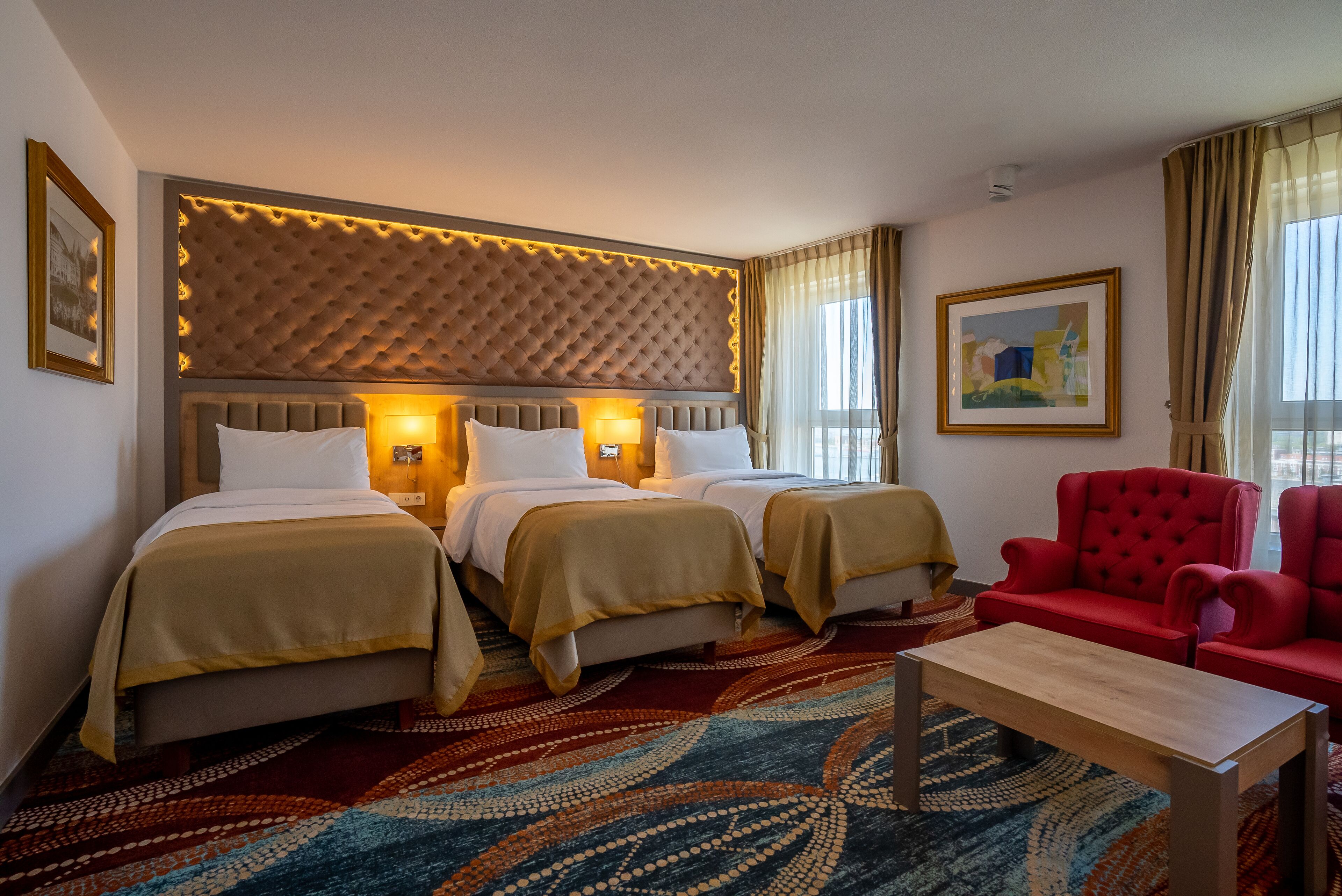 A hotel room with two beds, a red armchair, a wooden coffee table, and a patterned carpet.