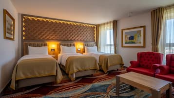 A hotel room with two beds, a red armchair, a wooden coffee table, and a patterned carpet.