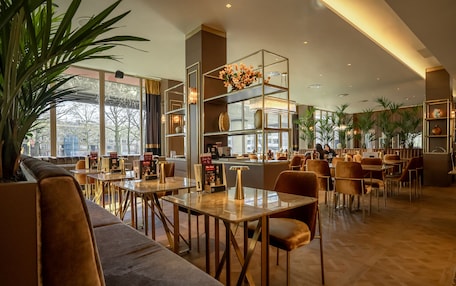 A modern restaurant with high ceilings, large windows, and a variety of seating options including tables and sofas.