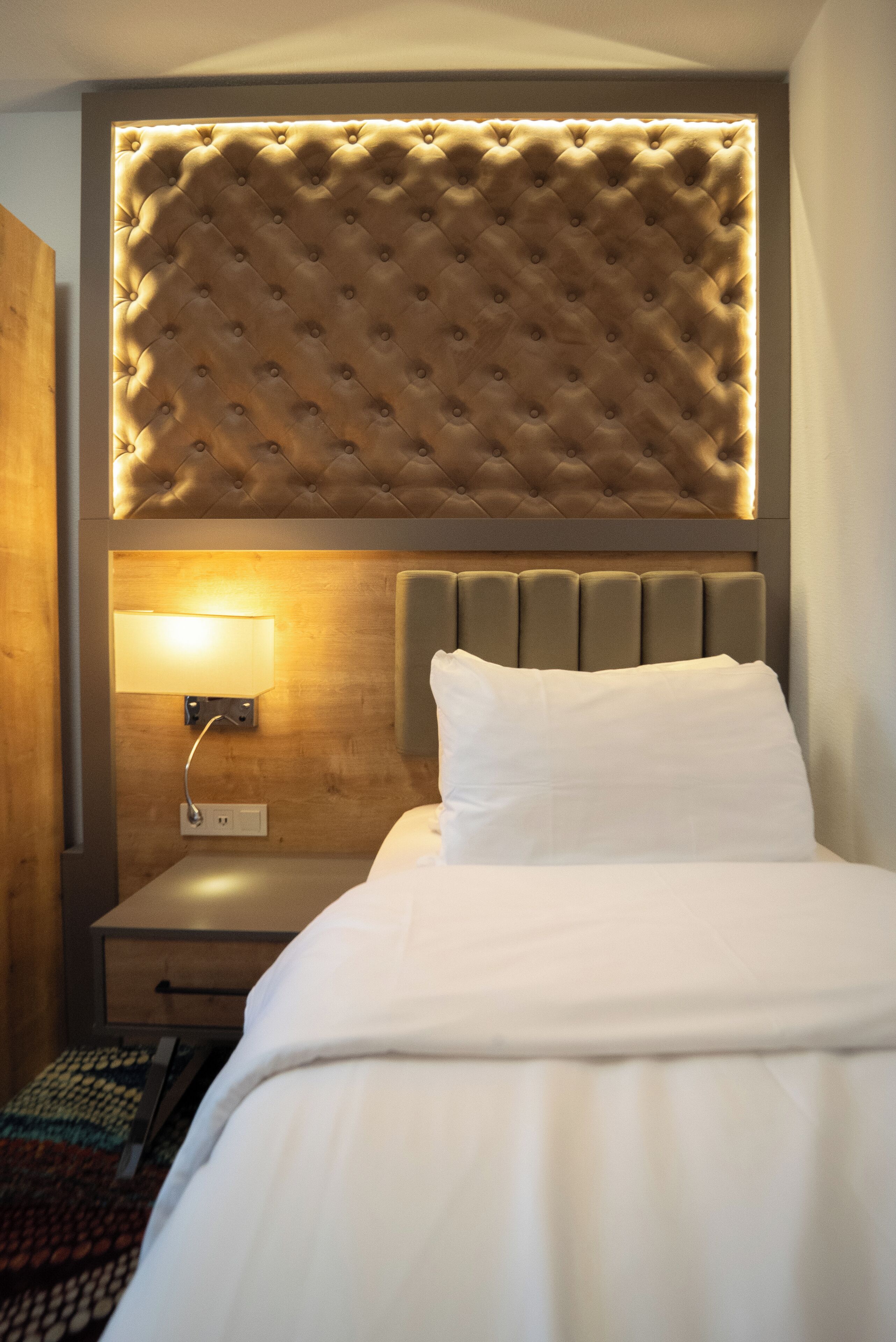 A neatly made bed with a tufted headboard, a bedside lamp, and a wooden nightstand.