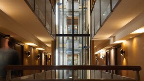 A modern hotel corridor with a central elevator, glass walls, and a wooden handrail. - Art Hotel Rotterdam (Rotterdam)