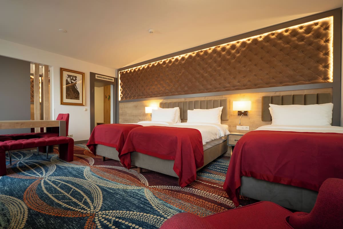 A hotel room with two beds, a bench, and a patterned carpet.