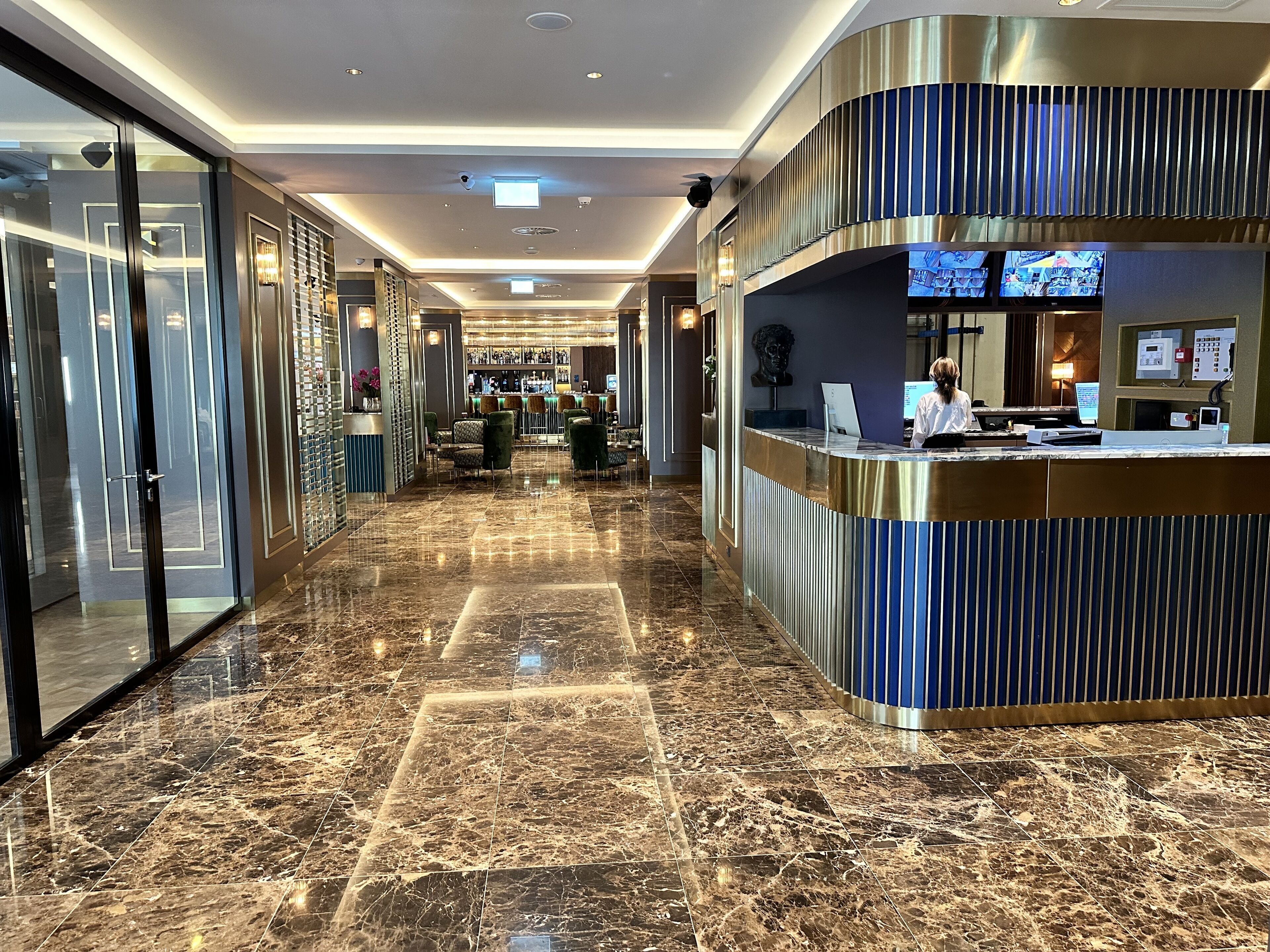 A hotel lobby with a reception desk, seating area, and a bar.
