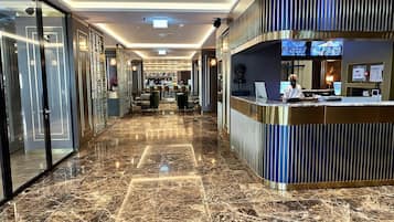 A hotel lobby with a reception desk, seating area, and a bar.