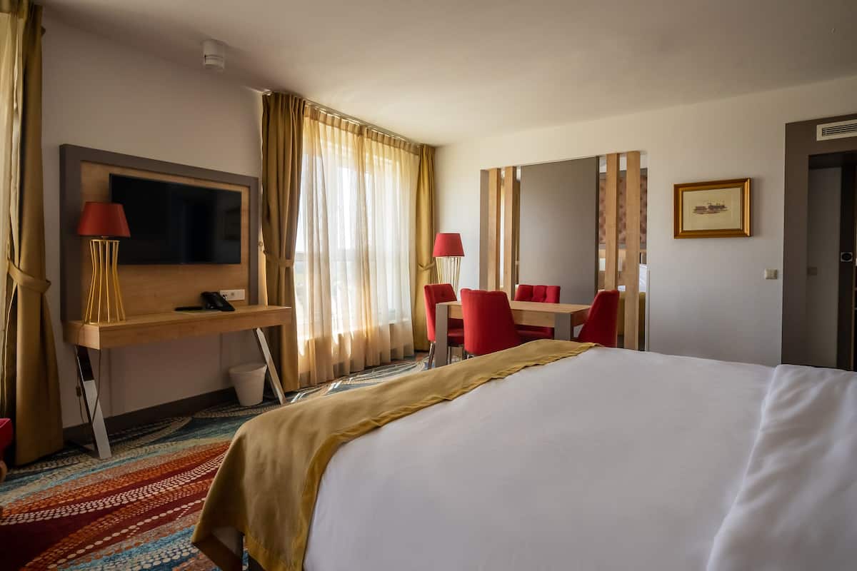 A hotel room with a large bed, a desk with a chair, a television, and a mirror.