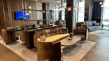 A modern hotel lobby with a plush seating area, a reception desk, and a large flat-screen TV.