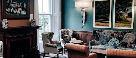 A living room with a chandelier, patterned furniture, a fireplace, and artwork on the walls.