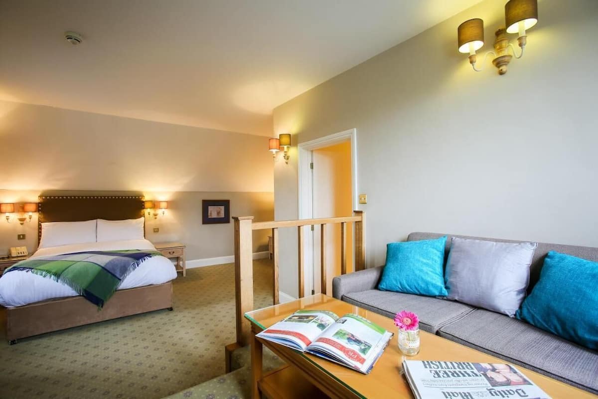Ein Hotelzimmer mit einem Bett, einem Sofa, einem Tisch mit einer Zeitschrift und Wandleuchten.