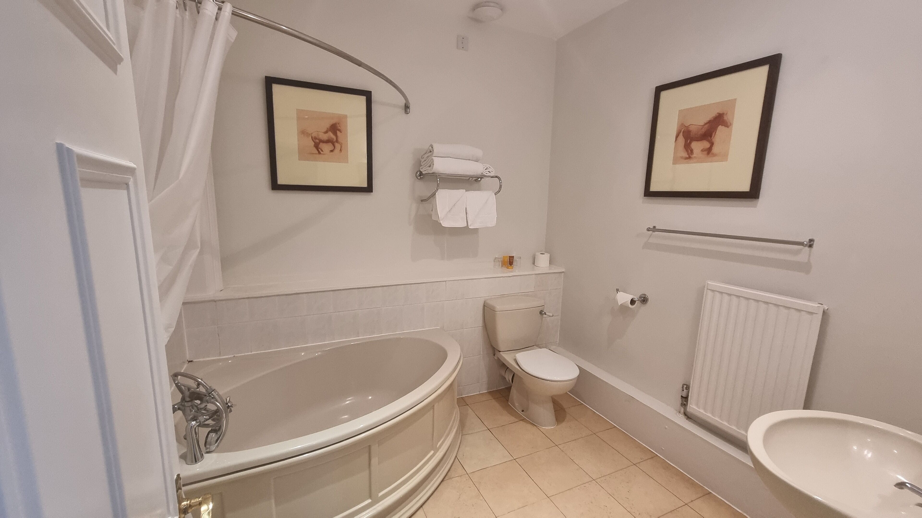 A bathroom with a bathtub, toilet, and sink. There are two framed pictures on the wall.