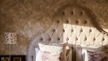 Camera da letto con testiera capitonata, numerosi cuscini, comodino con lampada e parete con superficie strutturata.