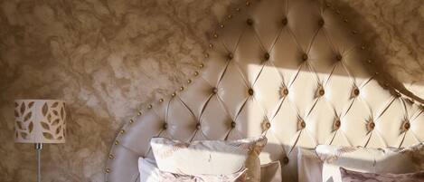 A bedroom with a tufted headboard, multiple pillows, a bedside table with a lamp, and a textured wall.