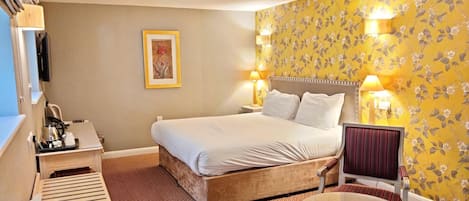 Ett hotellrum med en säng, sänglampor, ett litet bord, en stol och ett skrivbord med en telefon.