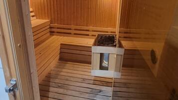 Una sala de sauna con paredes y bancos de madera, un banco con una toalla y un pequeño calentador.
