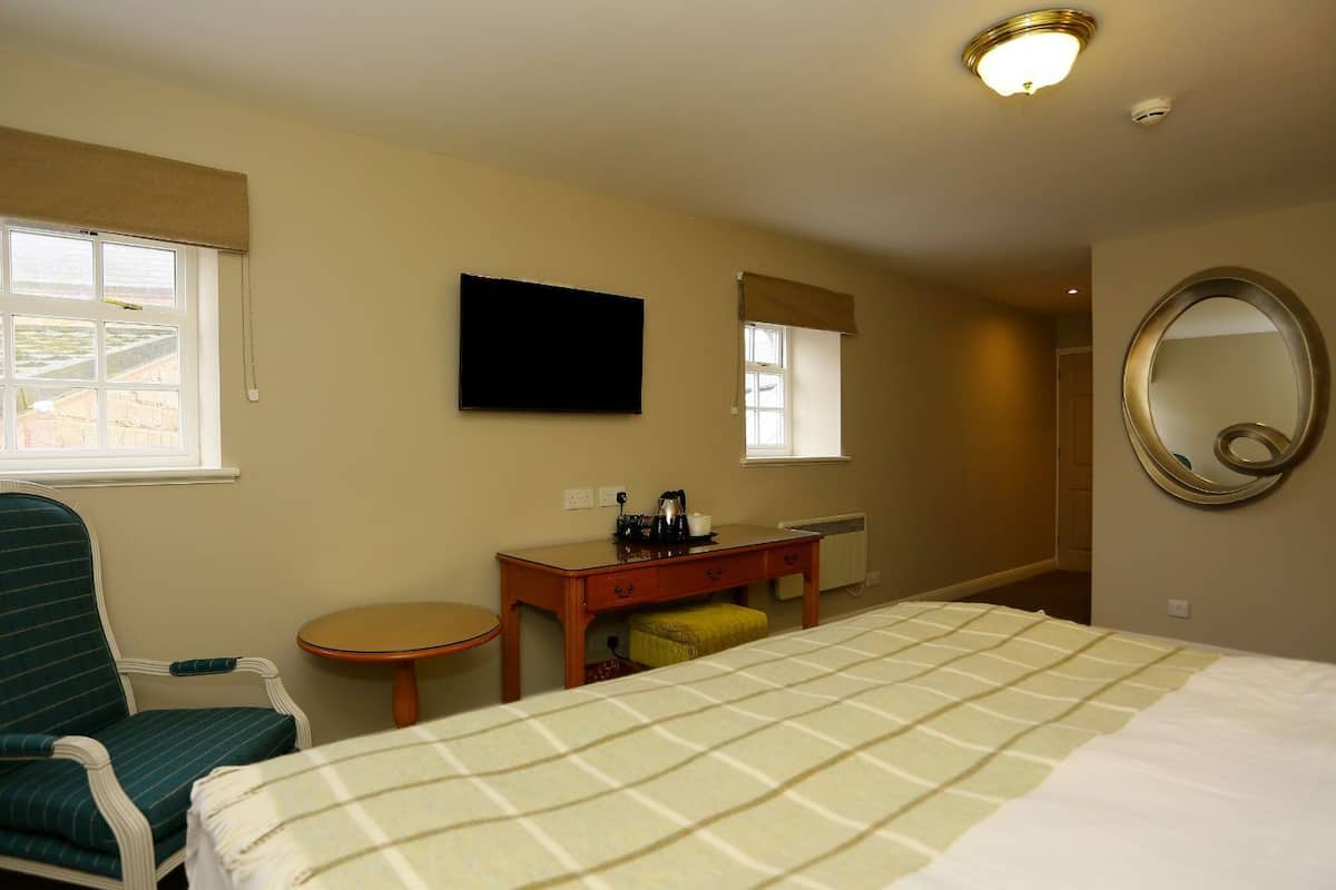 Ein Hotelzimmer mit einem Bett, einem Schreibtisch, einem Stuhl, einem runden Tisch, einem Fernseher, einem Spiegel und zwei Fenstern mit Jalousien.