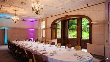 A formal dining room with a long table set for a meal, large windows, and classic chandeliers.