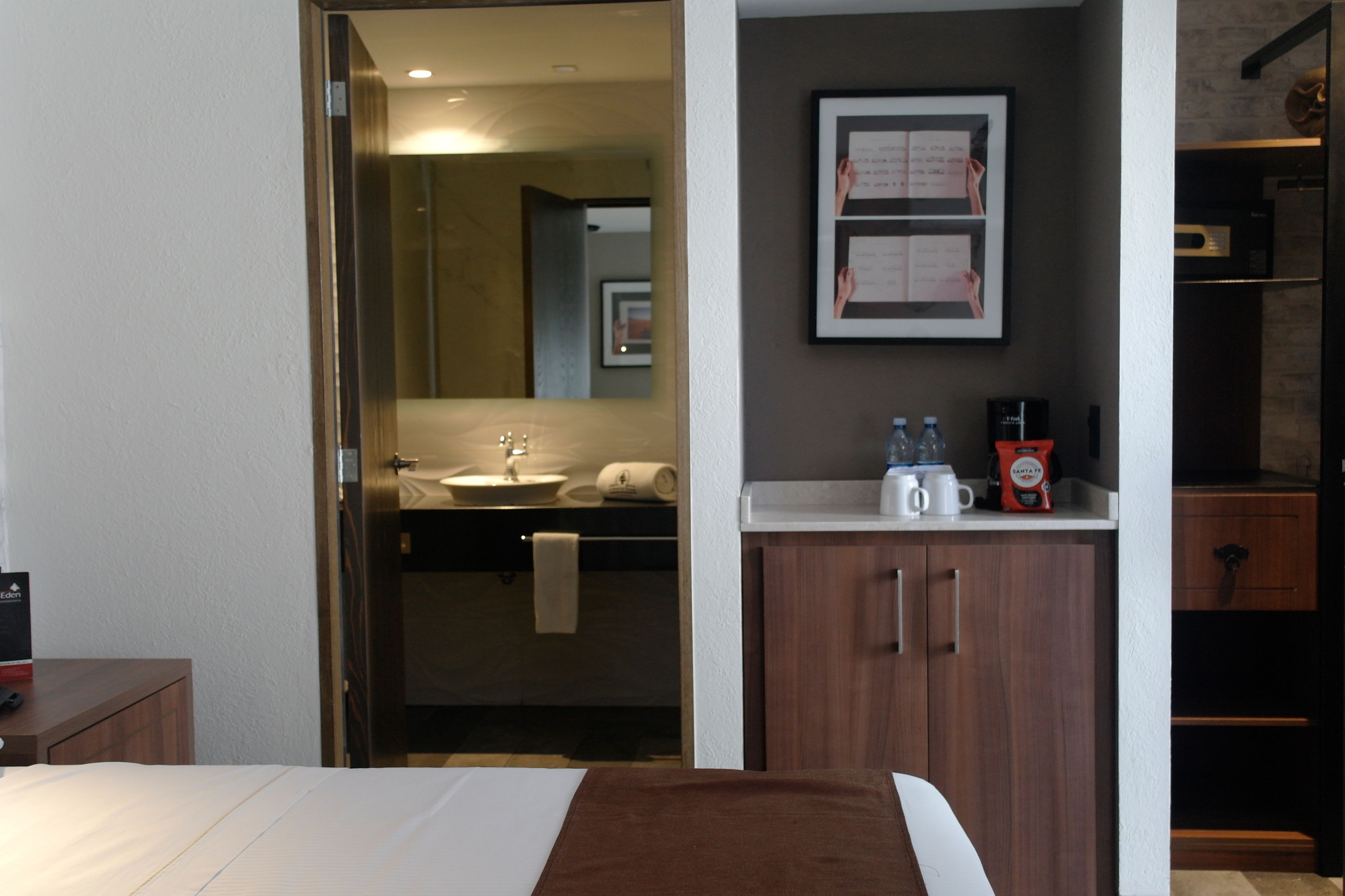 A hotel room with a bed, a bathroom with a sink, and a coffee machine on the counter.