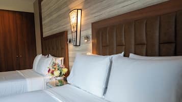 A hotel room with two beds, a wooden headboard, a wall-mounted light fixture, and a nightstand with a vase of flowers.