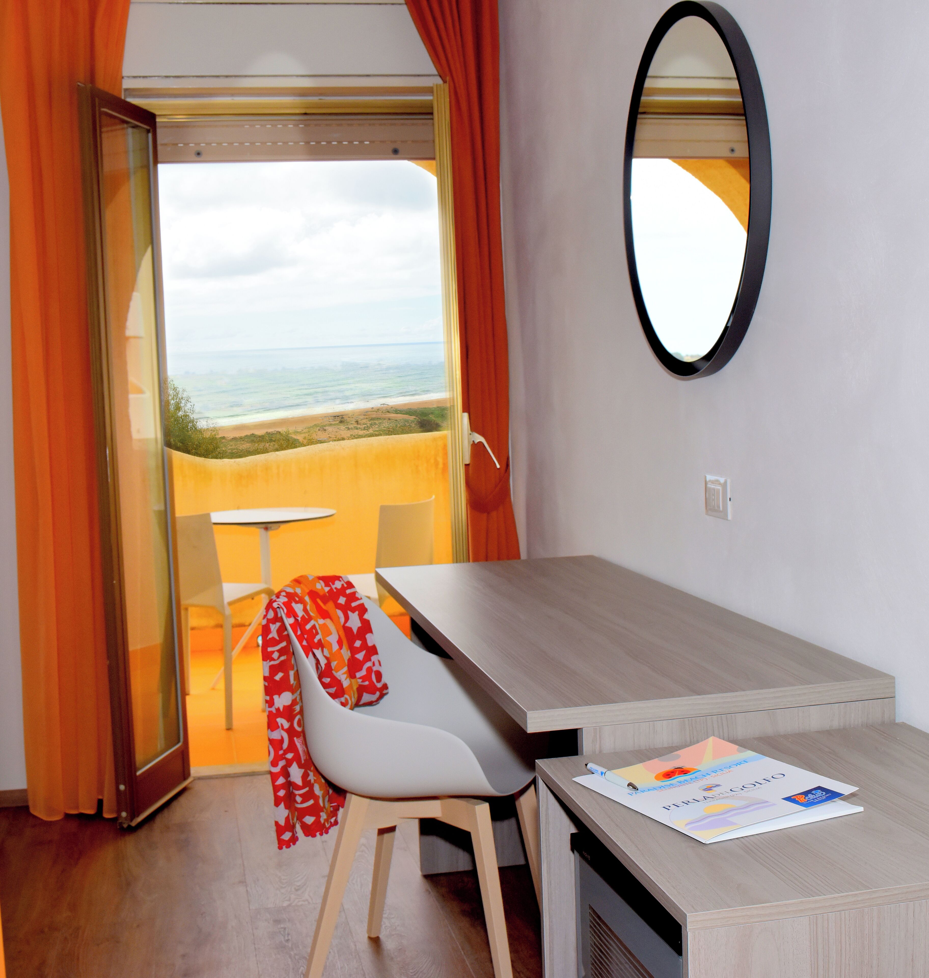 A room with a view of the beach, a table, a chair, and a mirror.