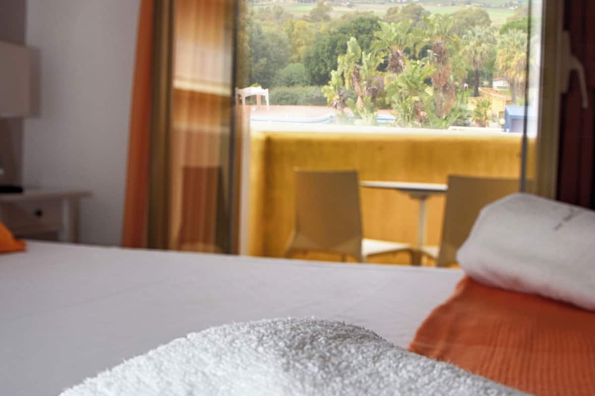 Habitación de hotel con cama, vistas por una ventana y balcón con sillas.