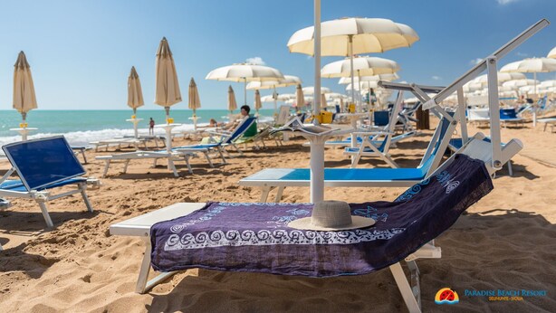 A beach with rows of sun loungers and umbrellas, some with beach towels and hats. - Paradise Beach Resort (Castelvetrano)