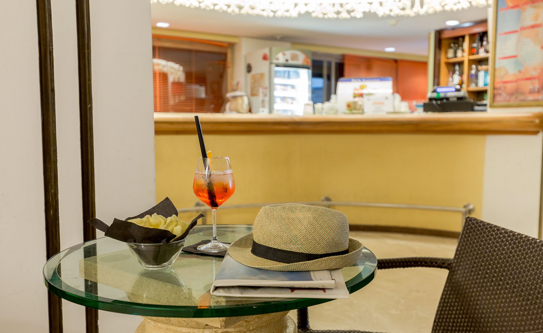 A glass table with a drink, a hat, and a bowl of chips.