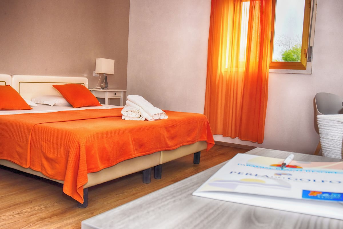 Habitación de hotel con cama, mesita de noche, lámpara, ventana con cortinas y una silla.