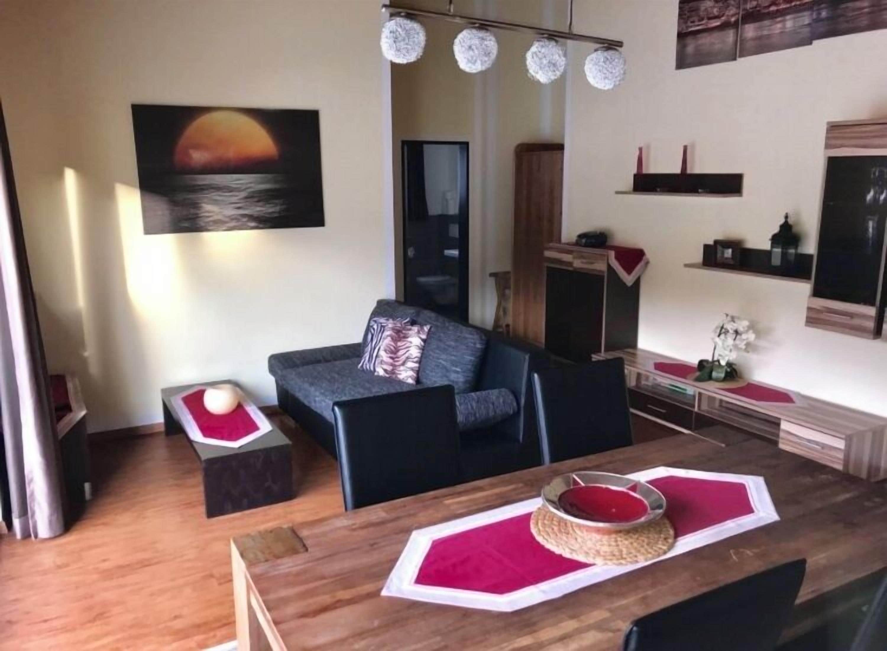 A modern living room with a sofa, a dining table with placemats, a painting of a sunset, and a cabinet.