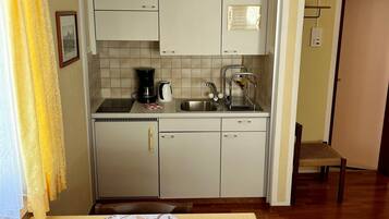 A compact kitchen with white cabinets, a sink, and a coffee maker. A dining table with a placemat and a vase is in the foreground.