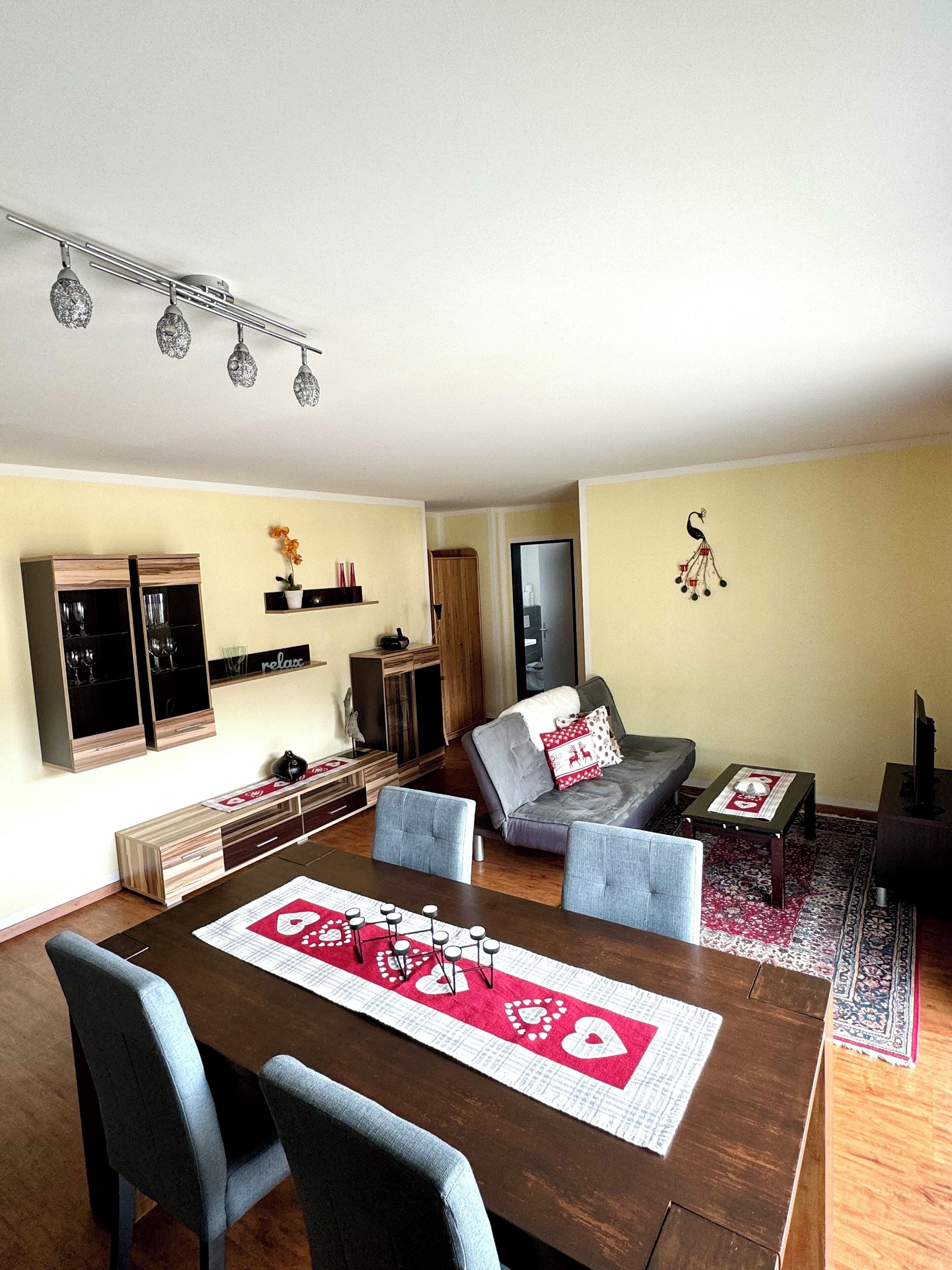 Una sala de estar moderna con comedor, que incluye una mesa de madera, sillas y un sofá con cojines decorativos.