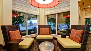A seating area with wicker chairs and a round ottoman, large windows with views, and a red pendant light. - Hilton Garden Inn Toronto/Burlington (Burlington)