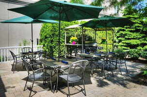 Un patio al aire libre con mesas y sillas de metal, sombrillas verdes y una parrilla.