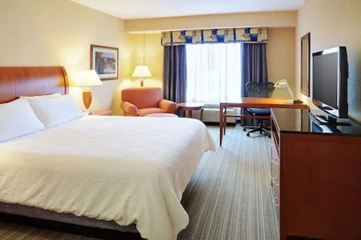 A hotel room with a large bed, a desk, a chair, a television, and a window with curtains.