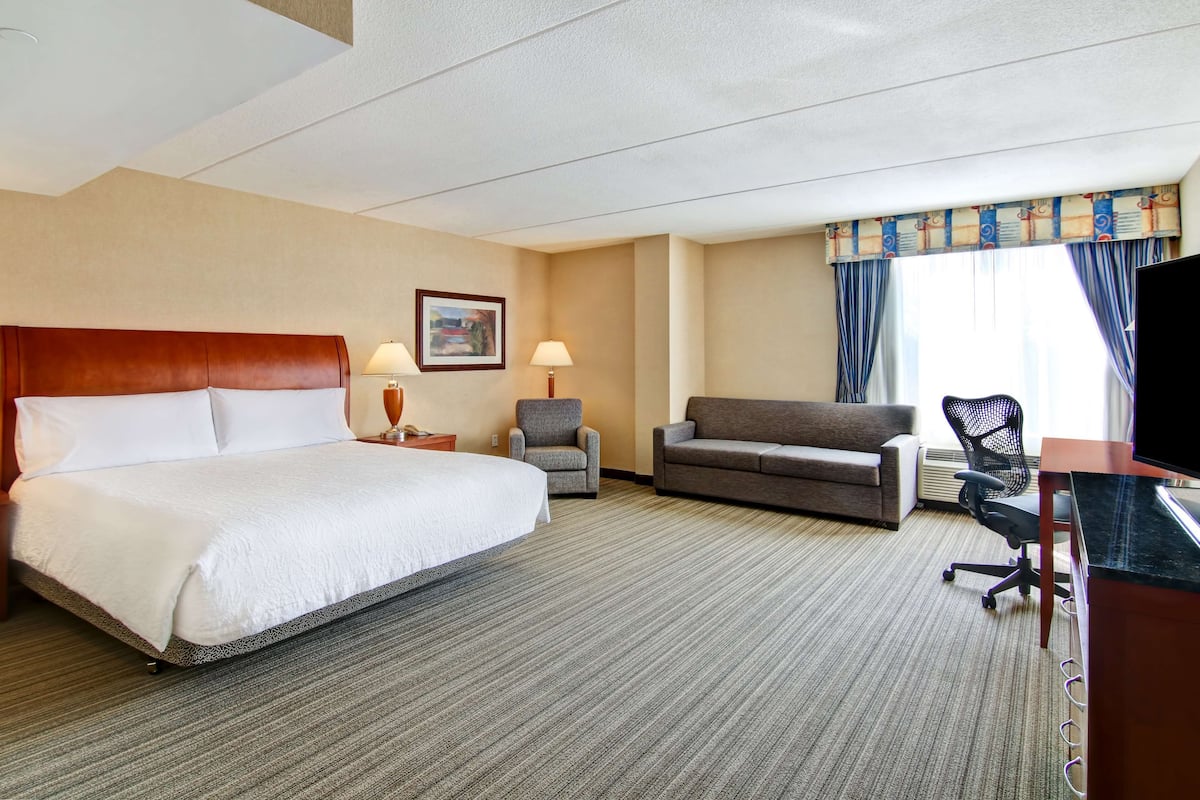 A hotel room with a large bed, a sofa, a desk with a computer, a chair, and a TV.