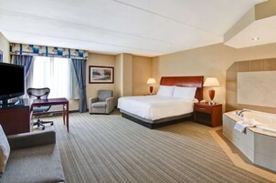 Habitación de hotel con cama, escritorio con silla, televisor, lámpara de escritorio, mesita de noche y bañera.