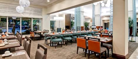 A spacious dining area with multiple tables and chairs, large windows, and decorative hanging lights.