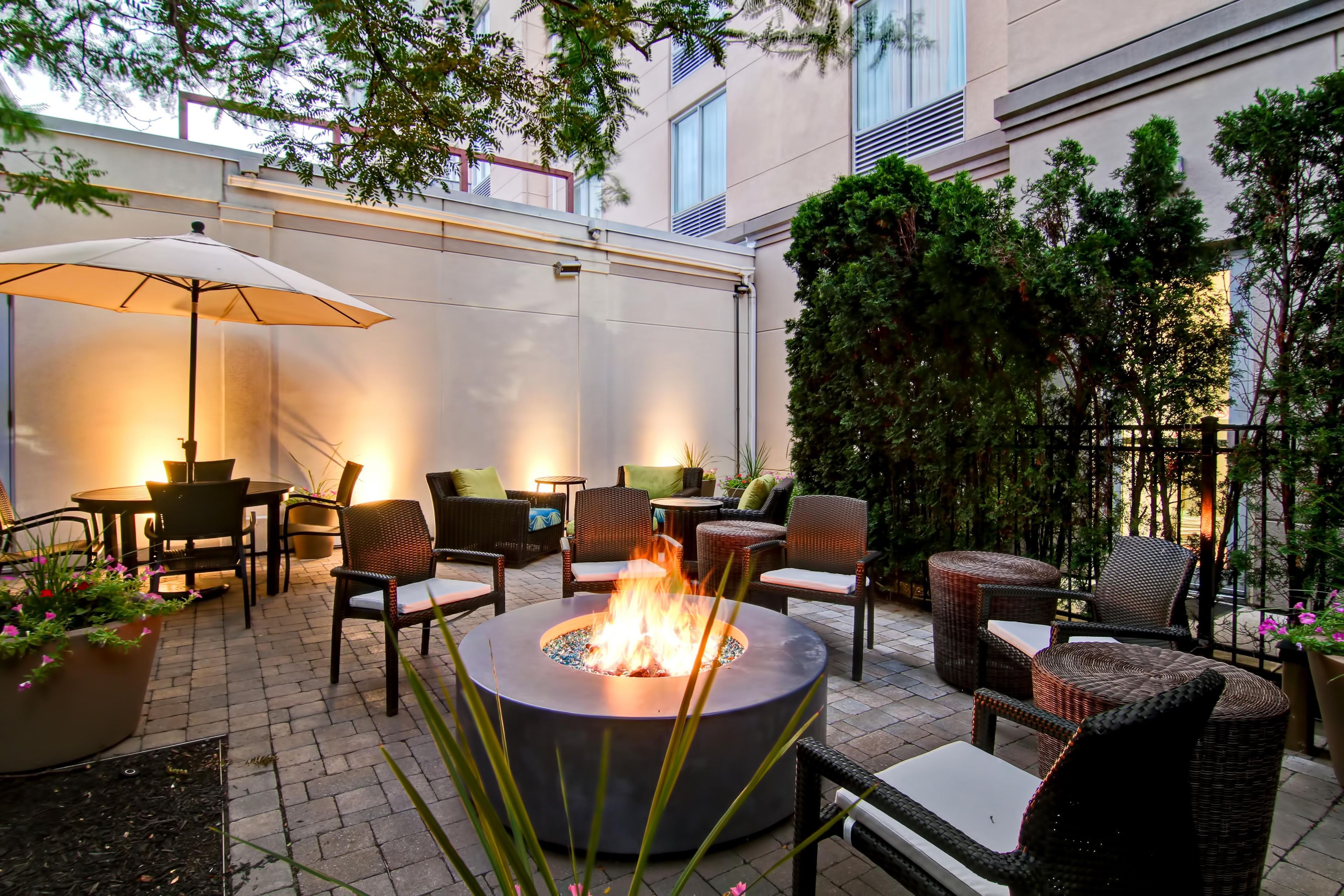 An outdoor patio with a round fire pit, wicker furniture, and a large umbrella.