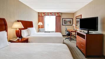 A hotel room with two beds, a desk, a television, and a lamp.