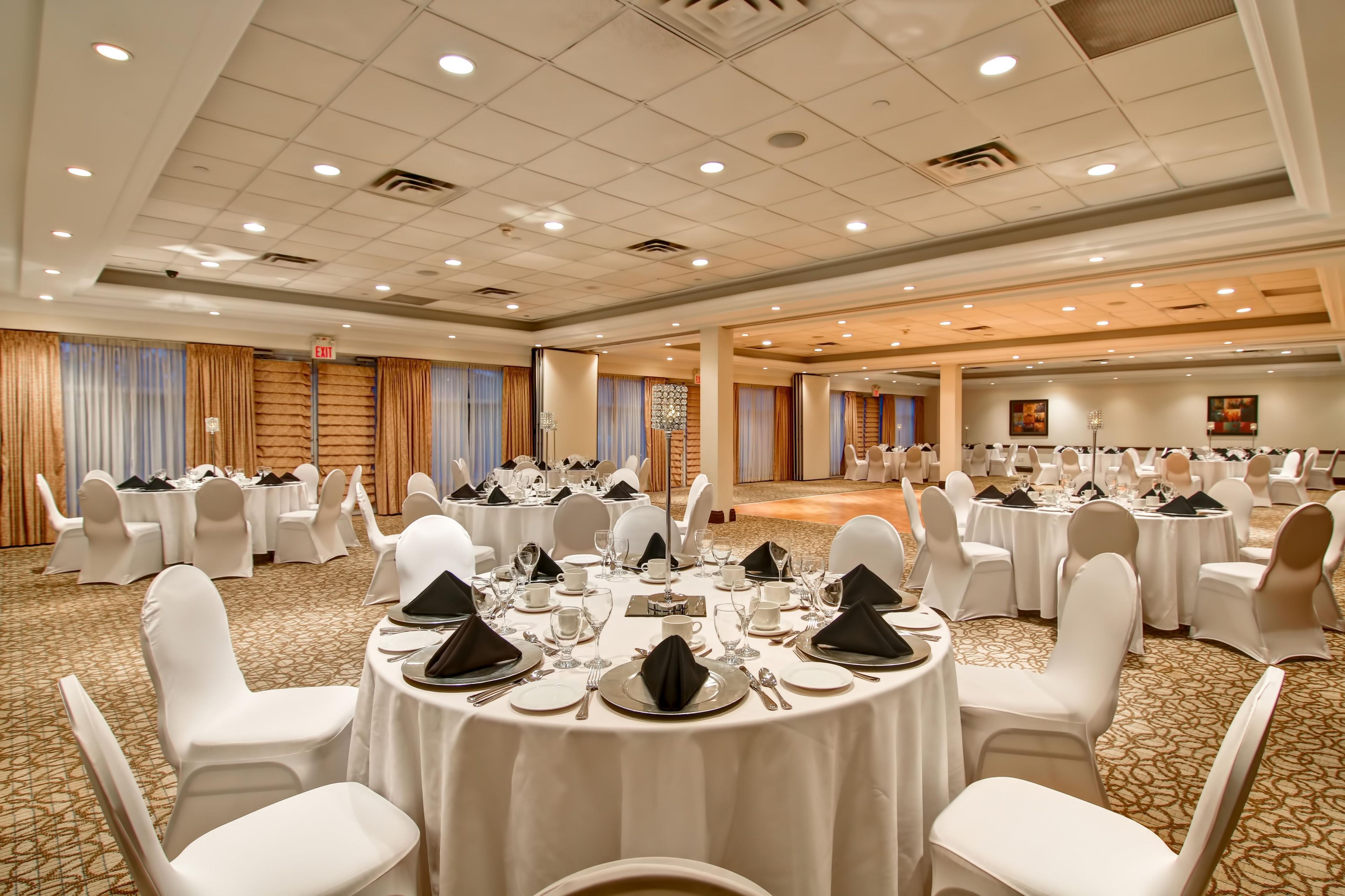 A banquet hall with round tables set for dining, white chairs, and a carpeted floor.