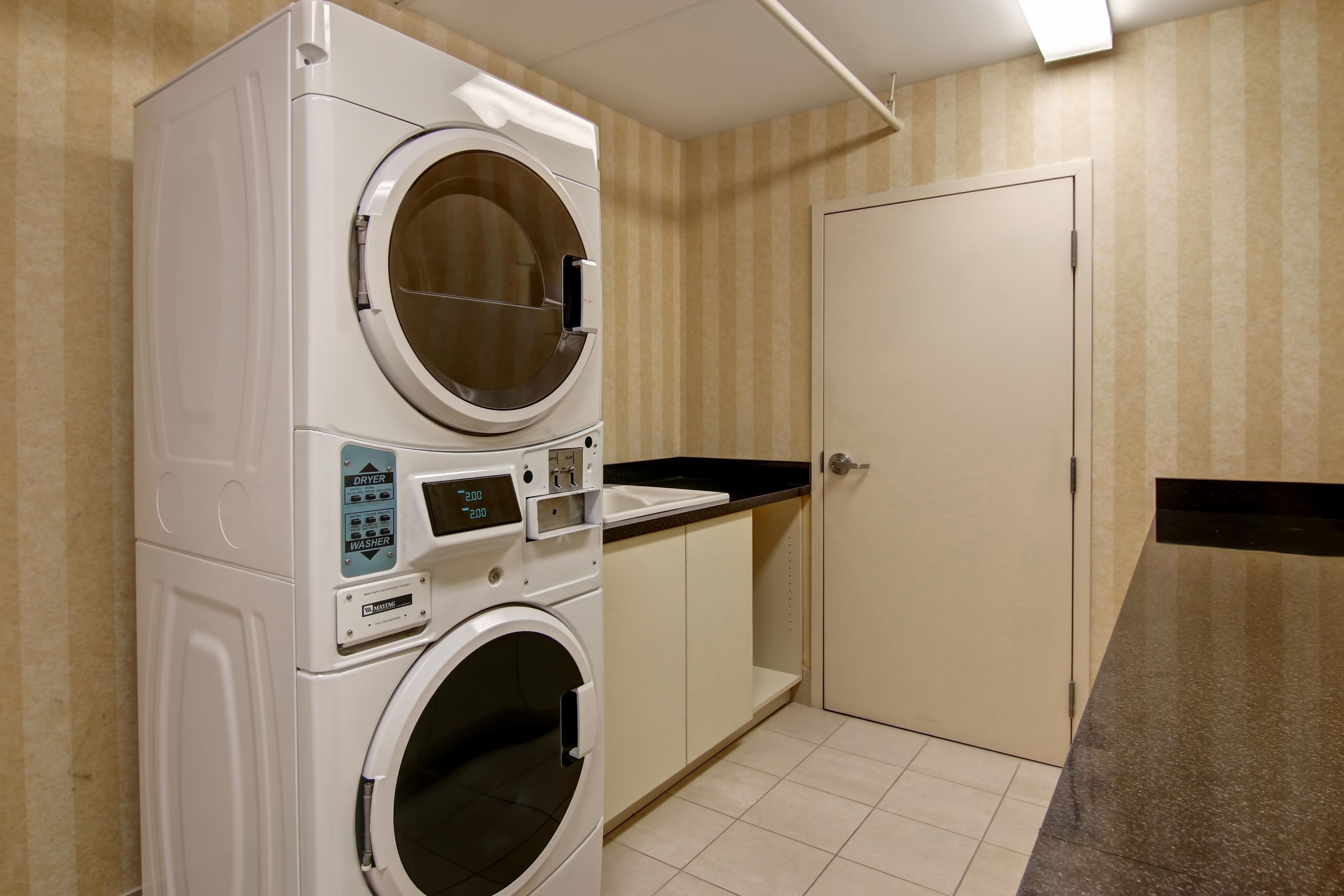 A laundry room with a stacked washer and dryer, a countertop, and a door.