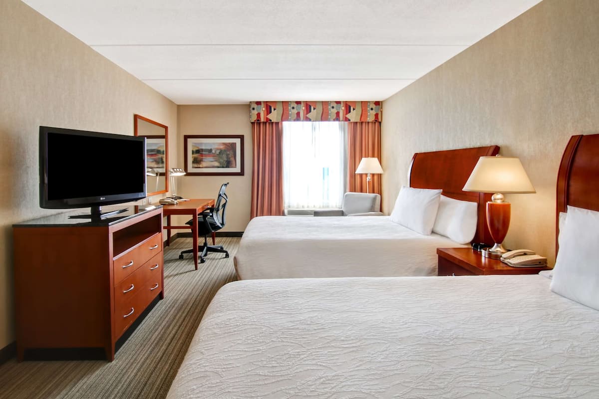 A hotel room with two beds, a TV, a desk, and a chair.