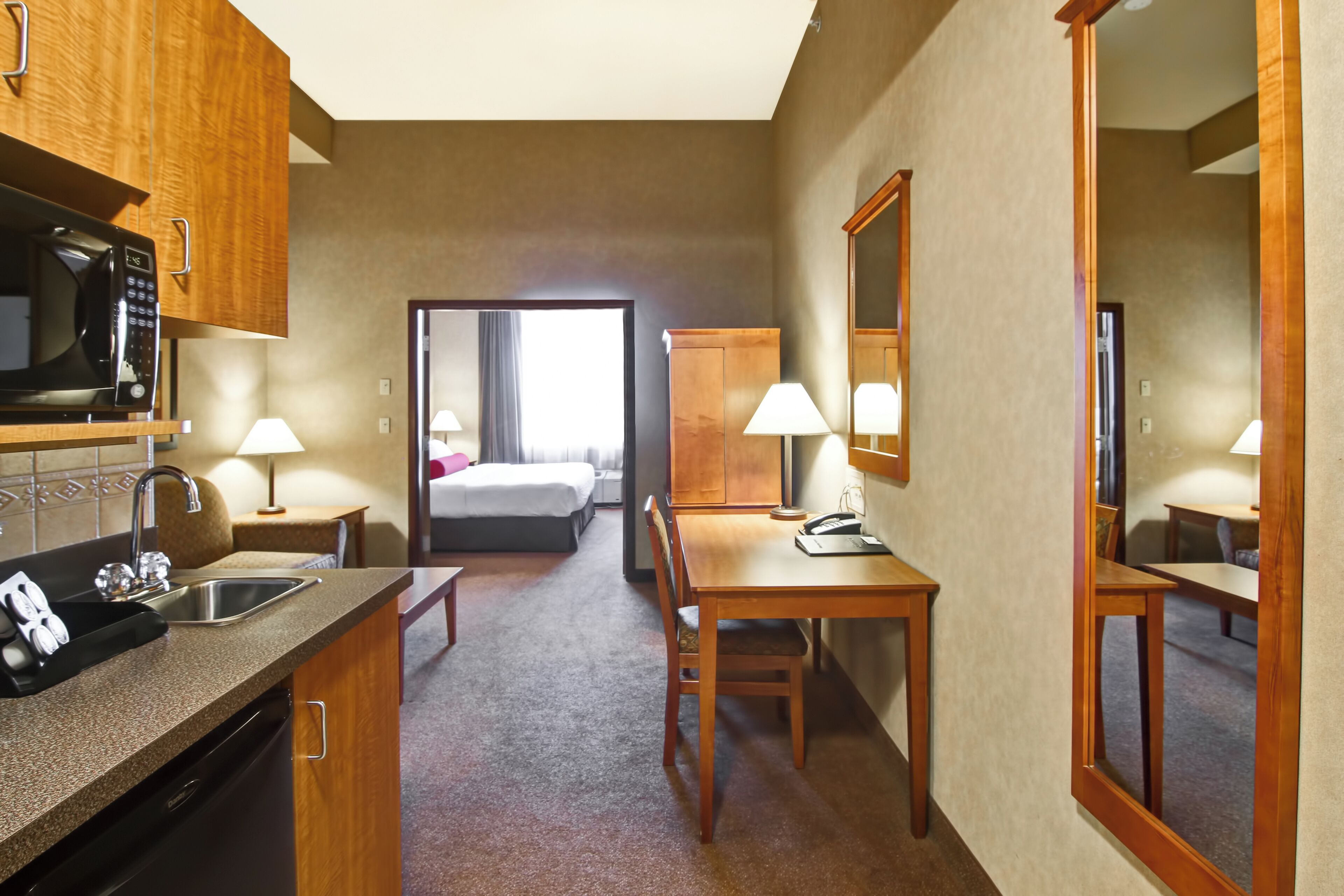 Una habitación de hotel con kitchenette, una cama, un escritorio y un espejo.