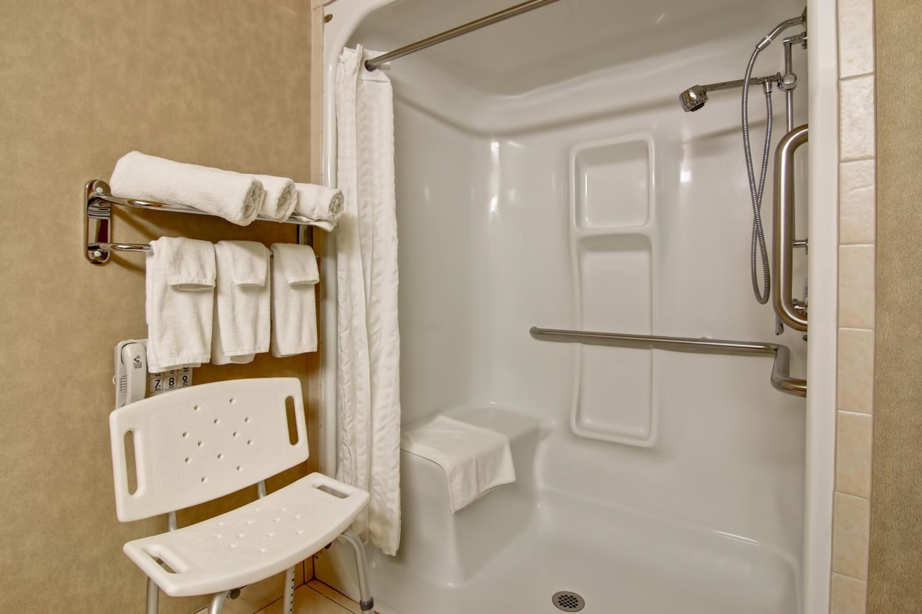 Un angolo doccia con porta in vetro, un portasacchi biancastro, una panca bianca e un tavolino bianco.
