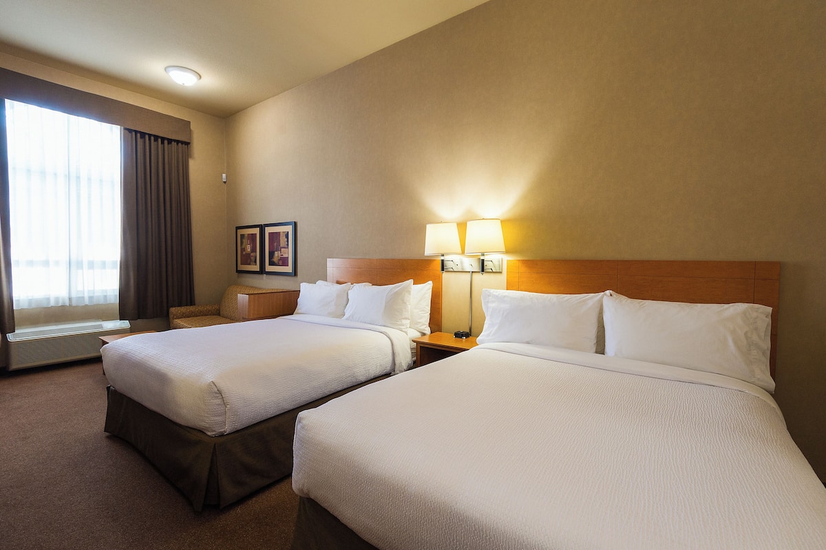 Habitación de hotel con dos camas, un ventanal con cortinas, una lámpara de pared y un cuadro en la pared.