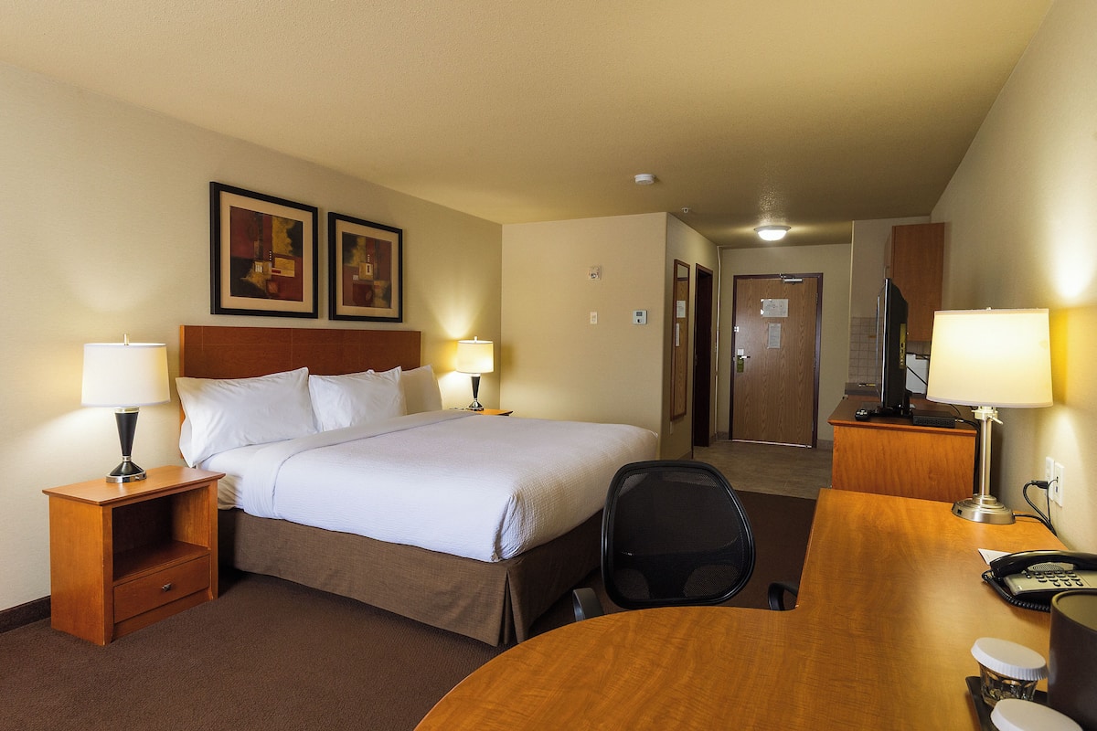 Una habitación de hotel con una cama, dos lámparas de noche, un escritorio con teléfono y una silla.