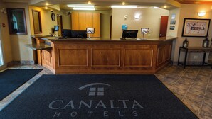 A reception area with a wooden reception desk, two computer monitors, a clock, and a framed picture on the wall. - Canalta Hotel Provost (Provost)