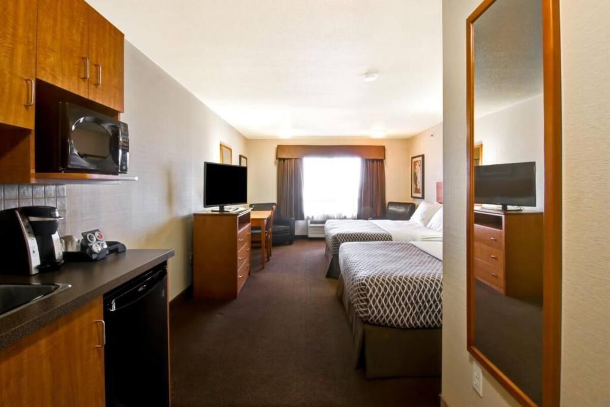 Habitación de hotel con kitchenette, dos camas, televisor y un espejo grande.