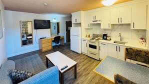 Un espacio habitable compacto con kitchenette, comedor y zona de estar con sofá y una pequeña mesa.