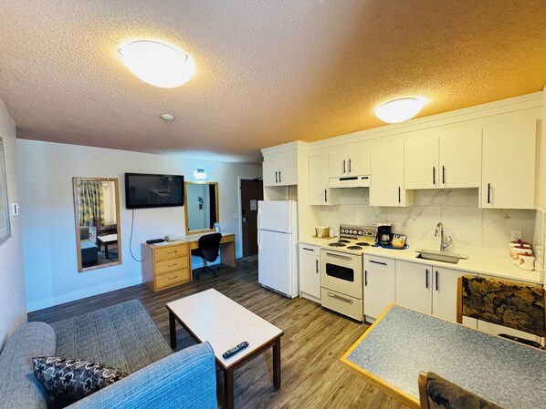 Un espacio habitable compacto con kitchenette, comedor y zona de estar con sofá y una pequeña mesa.